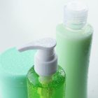 Green And White Shampoo, Conditioner, And Moisturizer Bottles With Water Pouring On Them